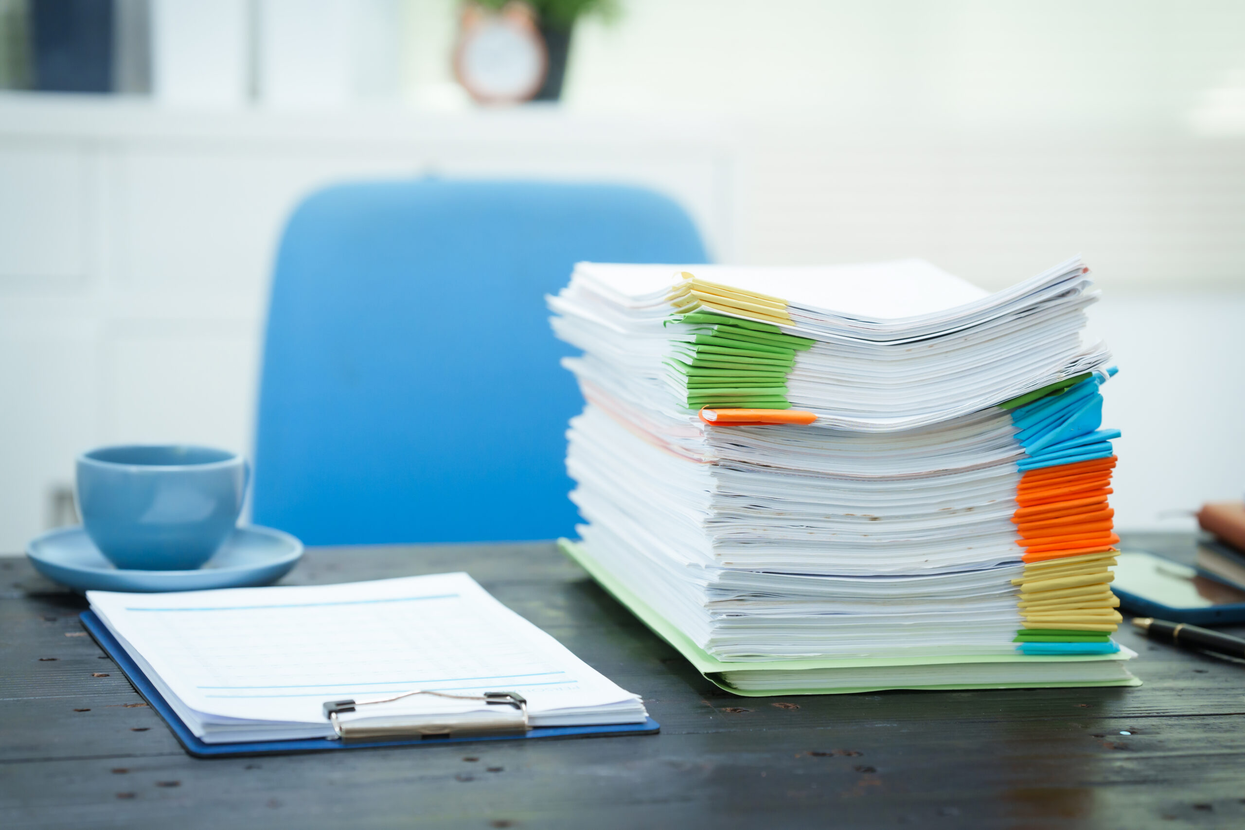 An empty office desk is cluttered with numerous documents scattered coffee cups.The scene reflects
